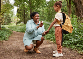 Side view portrait of black mother and daughter hiking together and using bug spray