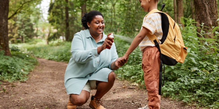 Side view portrait of black mother and daughter hiking together and using bug spray